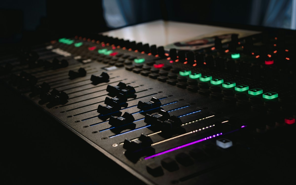 The faders, buttons and glowing level lights of a mixing console in a dimly lit studio